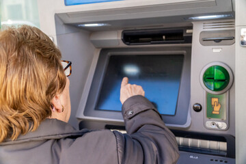 Elderly woman using the ATM in the city.