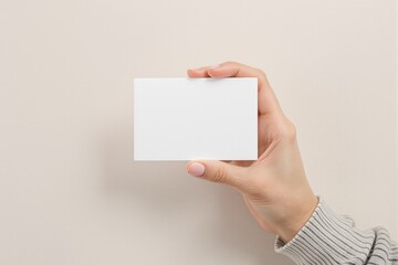 Obraz premium A hand grasps a blank white card, set against a neutral beige backdrop. Ideal for showcasing design concepts, copyspace, or branding ideas. Ai generative