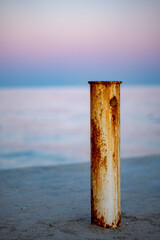 Close-up of rusted white metal poles on a concrete pier by the sea. Weathered maritime structure with corrosion details. Coastal landscape