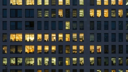 Nighttime view of a modern office building with illuminated windows showcasing diverse professionals at work Themes of productivity and urban living
