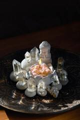 Buddha figurine with floral candle and crystal minerals on table, dark background. Magic altar....