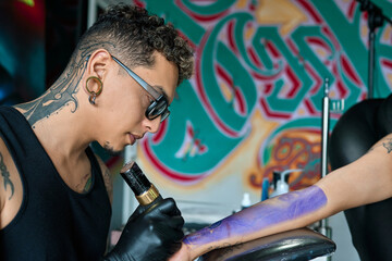 Tattoo artist carefully drawing a tattoo on the arm of a client in a professional studio, creating...