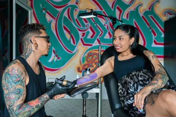 Professional tattoo artist wearing black gloves preparing purple ink for tattooing a smiling woman...