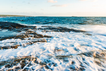 Coastal waves crashing against rocky shore in Sweden during golden hour