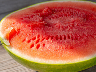 A close-up of a watermelon cut in half, with bright red flesh, green skin, and a fibrous texture....