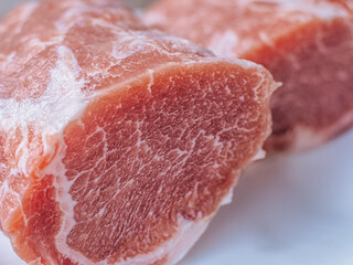 Close-up of a fresh raw pork chop with marbled fat, placed on a white plate. The rich texture and natural color highlight the meat's quality, ready for cooking preparation.