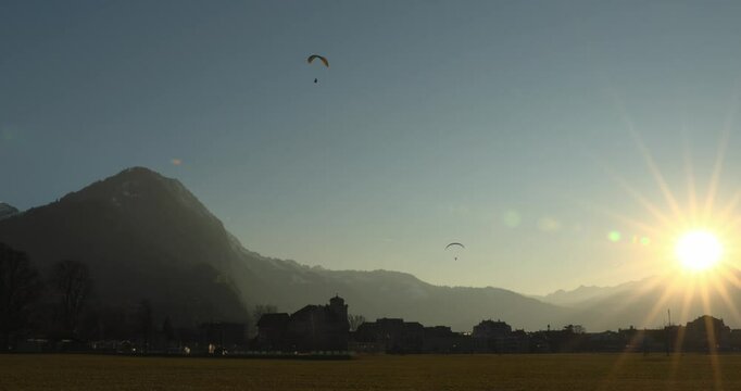 a paraglider soaring above majestic snow-capped mountains at sunset under a serene clear blue sky