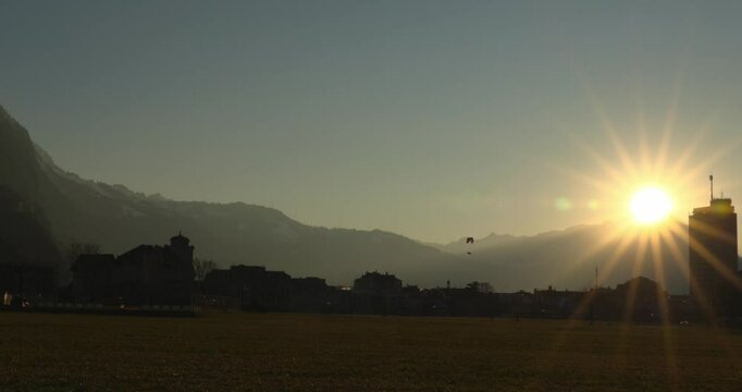 a paraglider soaring above majestic snow-capped mountains at sunset under a serene clear blue sky