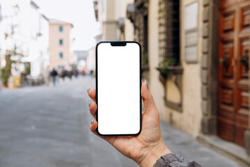 Mockup woman's hand holding using smart phone with white blank screen POV at on the background of a house on the street in Europe real estate  rent, mobile app design and advertising, online marketing