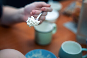 hand holding a spoon filled with creamy white cottage cheese, ready to be enjoyed. Perfect for health-conscious eating and dairy product themes