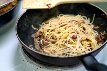 Thin spaghetti with tender chunks of stewed beef is being heated in a skillet on an electric stove, showcasing a delicious and hearty meal preparation