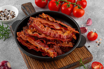 Fried slices of bacon for breakfast in a cast iron pan with tomatoes, garlic, rosemary and spices...