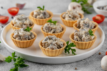 Mini tartlets with mushrooms in a cream sauce, with cheese, garlic and herbs on a white plate on a gray concrete background.