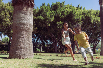 Fototapeta premium Understood, here it is: Joyful Young Mother Runs and Plays with Her Four-Year-Old Son in the Park