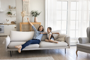 Celebrate new beginning. Excited young mom little child daughter rest on sofa at modern comfortable...