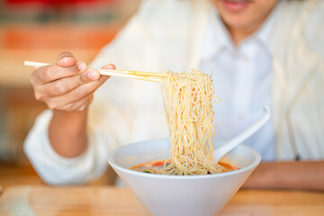 Crop anonymous female with chopsticks eating yummy ramen soup with noodles and meat in black bowl at ramen restaurant.