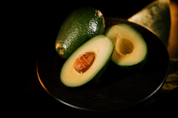 Fresh avocado halves placed on a rustic wooden board against a black background emphasizing the...