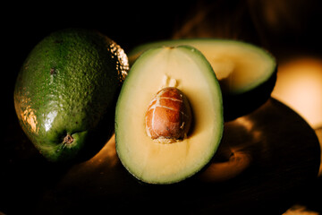 Whole fresh avocado and sliced half revealing smooth texture against a dark background highlighting its natural beauty