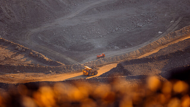 Banner industry, heavy industrial dump truck transports copper and gold ore in open pit mine, sunset.