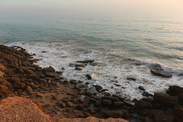 Ocean waves crashing on rocky coast at sunset, creating white foam