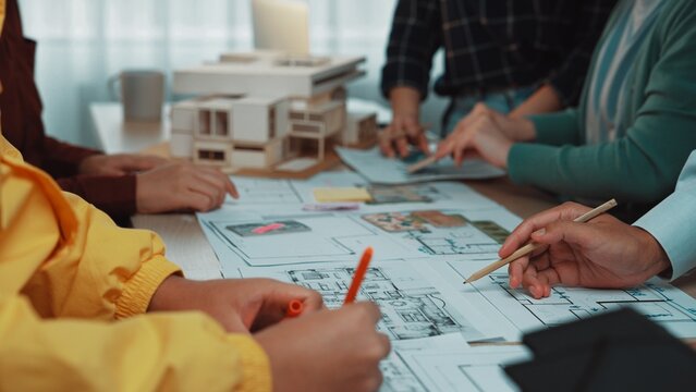 A group of professionals engaged in a collaborative architectural design session, actively discussing and sketching various concepts on detailed blueprints to enhance creativity. SACTR