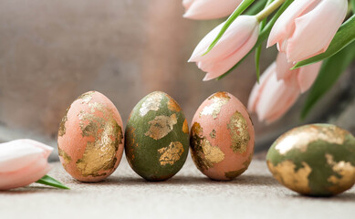 The concept of a bright Easter holiday. Delicate Easter eggs in pink, gold and green tones and delicate pink tulip flowers.