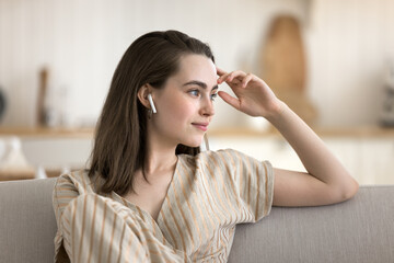 Modern tech for peace of mind. Portrait dreamy young female zoomer take break to rest on sofa listen to serene songs in true wireless earbuds enjoy audiobook nature sounds tracks find relaxation calm