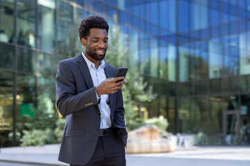 Successful businessman walking through the city with phone in hand. Joyful African American man in...