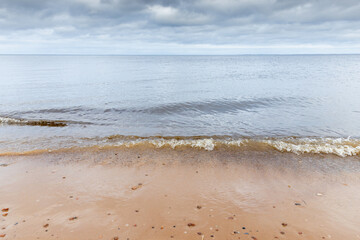 Calm waves gently lapping on a sandy beach, under overcast skies