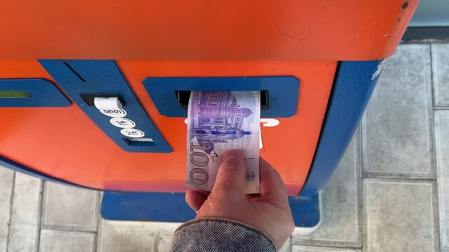 Horizontal 4K video close up. Male hand puts 100 GEL into blue orange ATM. Paper purple banknote. Cash money. Symbol of Georgian currency. Concept of salary, tax, bribe, pay loan. One hundred lari