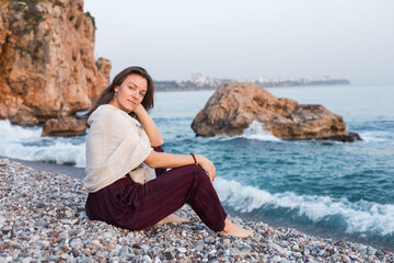 Woman relaxing on a peaceful beach during sunset near large rocks and gentle waves