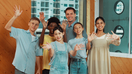 Smart teacher and diverse student standing while waving hand to camera. Skilled instructor with highschool children with mixed races in casual outfit greeting and smiling with cheerful. Edification.