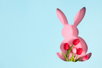 Easter background with bunny. A bright image of a silhouette of a pink bunny filled with tulips on a pastel blue background. Flat lay.