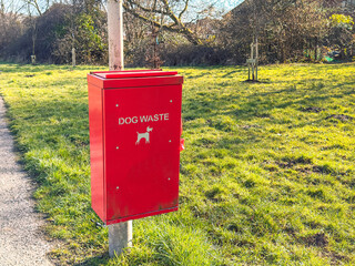 Metal bin for dog waste in a public park. No people.