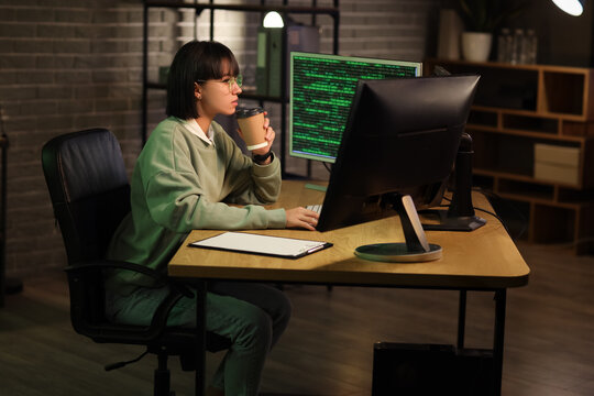 Female programmer with coffee cup working in office at night