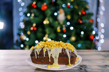 Traditional stollen with icing stands on a plate on the table against the backdrop of a sparkling...
