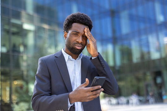 Upset and worried businessman with phone in hand looking at camera. African American man in business suit received online notification with bad news.