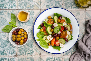 Greek salad of fresh cucumber, tomato, sweet pepper, lettuce, feta cheese and olives with olive oil on a blue tiles background. Healthy food, top view. High quality photo