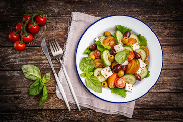 Greek salad of fresh cucumber, tomato, sweet pepper, lettuce, feta cheese and olives with olive oil on a wooden background. Healthy food, top view. High quality photo