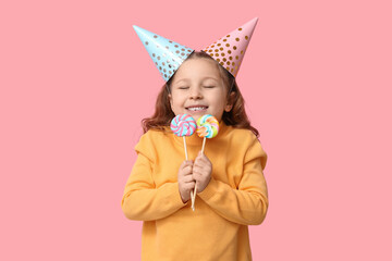 Cute little girl in holiday caps with lollipops on pink background