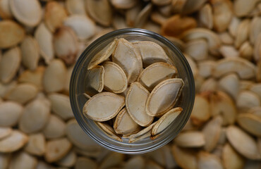Pumpkin seeds in a glass jar surrounded by a pile of seeds in cozy autumn setting