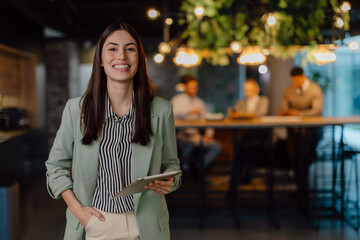 Confident Businesswoman Holding Tablet in Modern Office with Team in Background