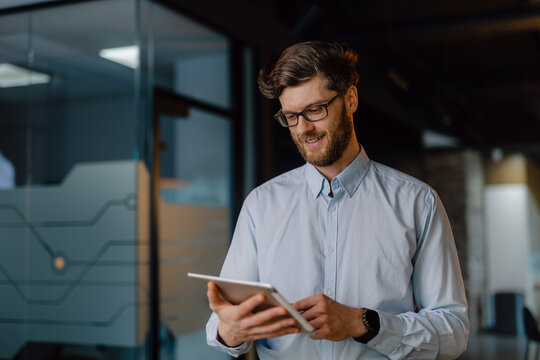 Smiling Professional Holding a Tablet in a Modern Office Environment