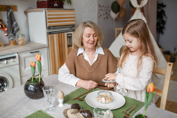 Elderly woman grandmother and little granddaughter joyfully set the table at home in the kitchen, learn etiquette