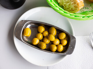 Appetites are waiting on table, light snack - bowl with pickled green olives. Traditional vegetable addition to main dishes, snacks and alcoholic beverages