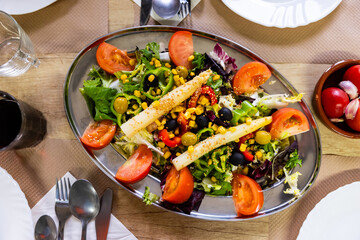 Plate of colorful appetizing salad of fresh greens, slices of tomato and peppers, corn and white asparagus, sprinkled with sesame seeds. Healthy appetizer concept