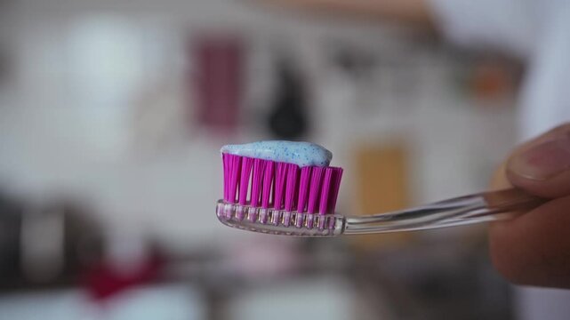 The paste from the tube is squeezed onto the purple bristles of a toothbrush.