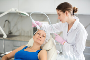 Young doctor use macromolecule atomizing pen for atomized nutrients to supplement and face skin nutrition for woman in cosmetology clinic. Professional moisturizing and rejuvenating hardware