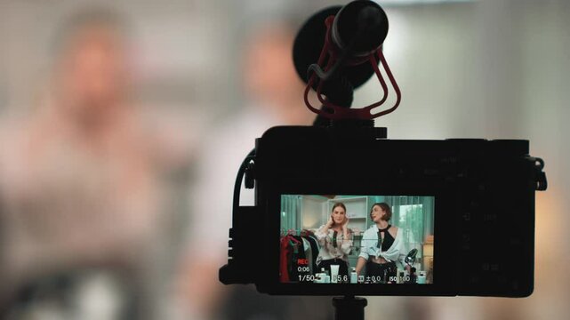 Rear view behide camera screen display two women influencer shoot vlog video review clothes prim social media or blog. Girls with apparel studio lighting for live streaming marketing recording session