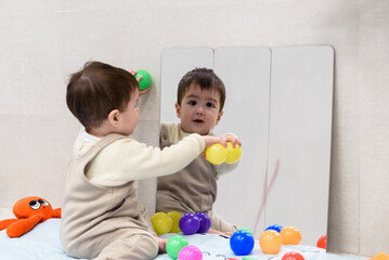 Baby boy playing with colorful balls and discovering himself in the mirror